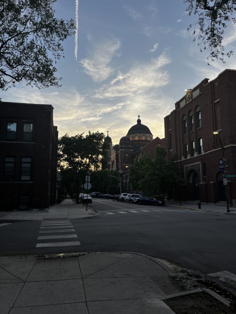 church illuminated by the sunset in a street in Chicago, with brick buildings around and an intersection right in front of the viewer