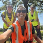 Three people smiling in image, Elizabeth on the left with a green hat, Andrea in the right in a green hat, and ren in the front with sunglasses. All three are in reflective vests.